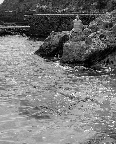 Quiet Times #41 by Jeremy Chin - Girl Sitting on the Rocks in Monterosso, Cinque Terre, Italy